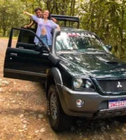 Casal acenando em pé na caminhonete 4x4 na mata