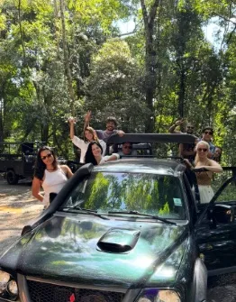 Turistas acenando em pé na caçamba da caminhonete 4x4 no meio da mata